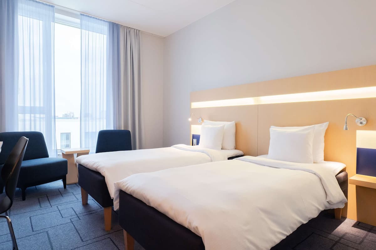 A hotel room with two beds, a desk, a chair, and a large window with curtains.