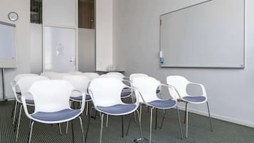 Een vergaderruimte met witte stoelen, een whiteboard en een klok aan de muur.