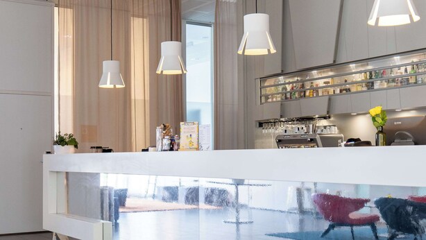 Een moderne hotelentree met een receptiebalie, een glazen scheidingswand en een bar.