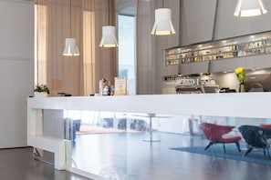 Un moderno vestíbulo de hotel con un mostrador de recepción, una mampara de vidrio y una zona de bar.