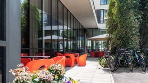Een terras met oranje stoelen en tafels, een rij fietsen en een bloembak met bloemen.