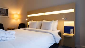 Habitación de hotel con una cama grande, una mesita de noche, una lámpara y una estantería con espejo.