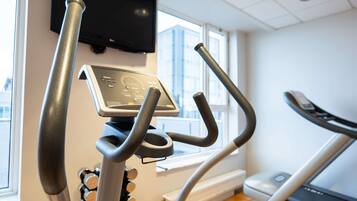 Un gimnasio con equipo de ejercicio, un panel de control y una ventana con vista a edificios.