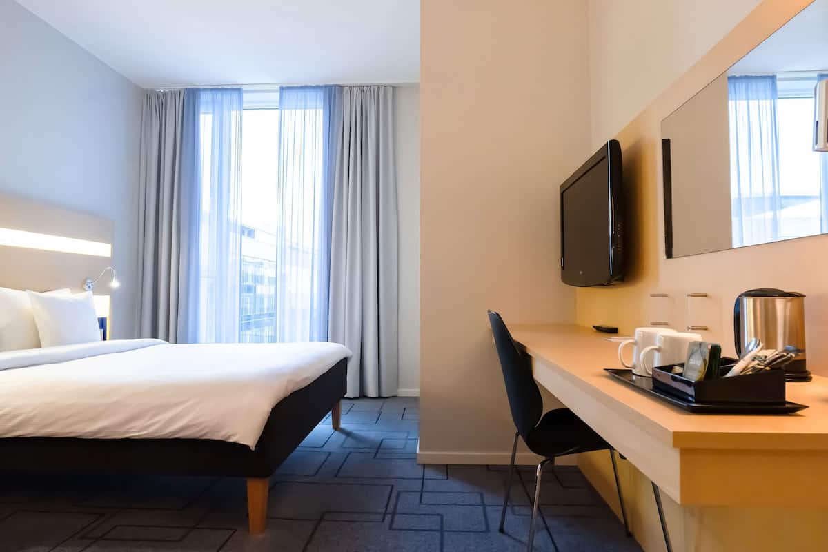 A hotel room with a bed, a desk with a chair, a television, and a coffee maker.