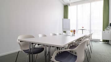 Un salón de conferencias con una mesa y sillas blancas, una pizarra y vistas a una cortina verde y una ventana.