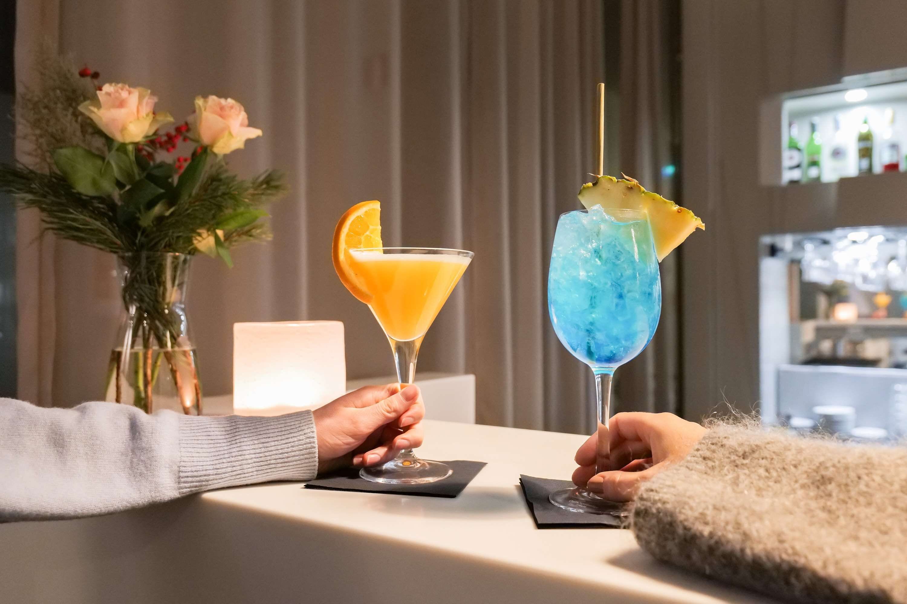 Two cocktails on a table with a vase of flowers in the background.