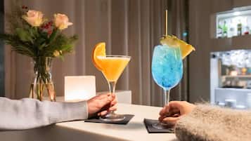 Two cocktails on a table with a vase of flowers in the background.