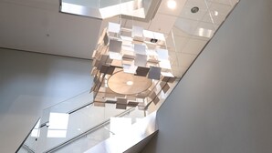 Een modern interieur met een glazen trap en een geometrisch plafondontwerp.