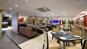 A modern restaurant with multiple dining areas, including booths and tables, and a visible kitchen area. - The Grace Hotel Near IGI Airport, New Delhi (New Delhi)