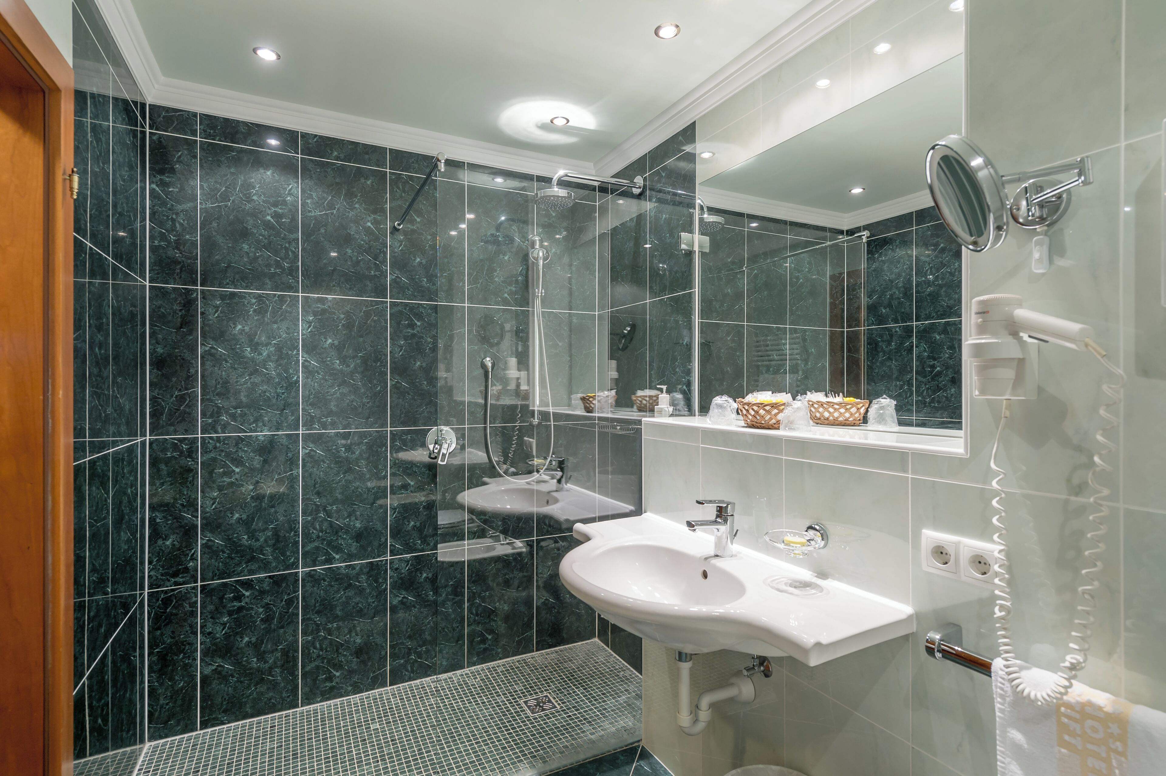 Une salle de bain moderne avec une douche à l’italienne en verre, un lavabo blanc et un grand miroir.