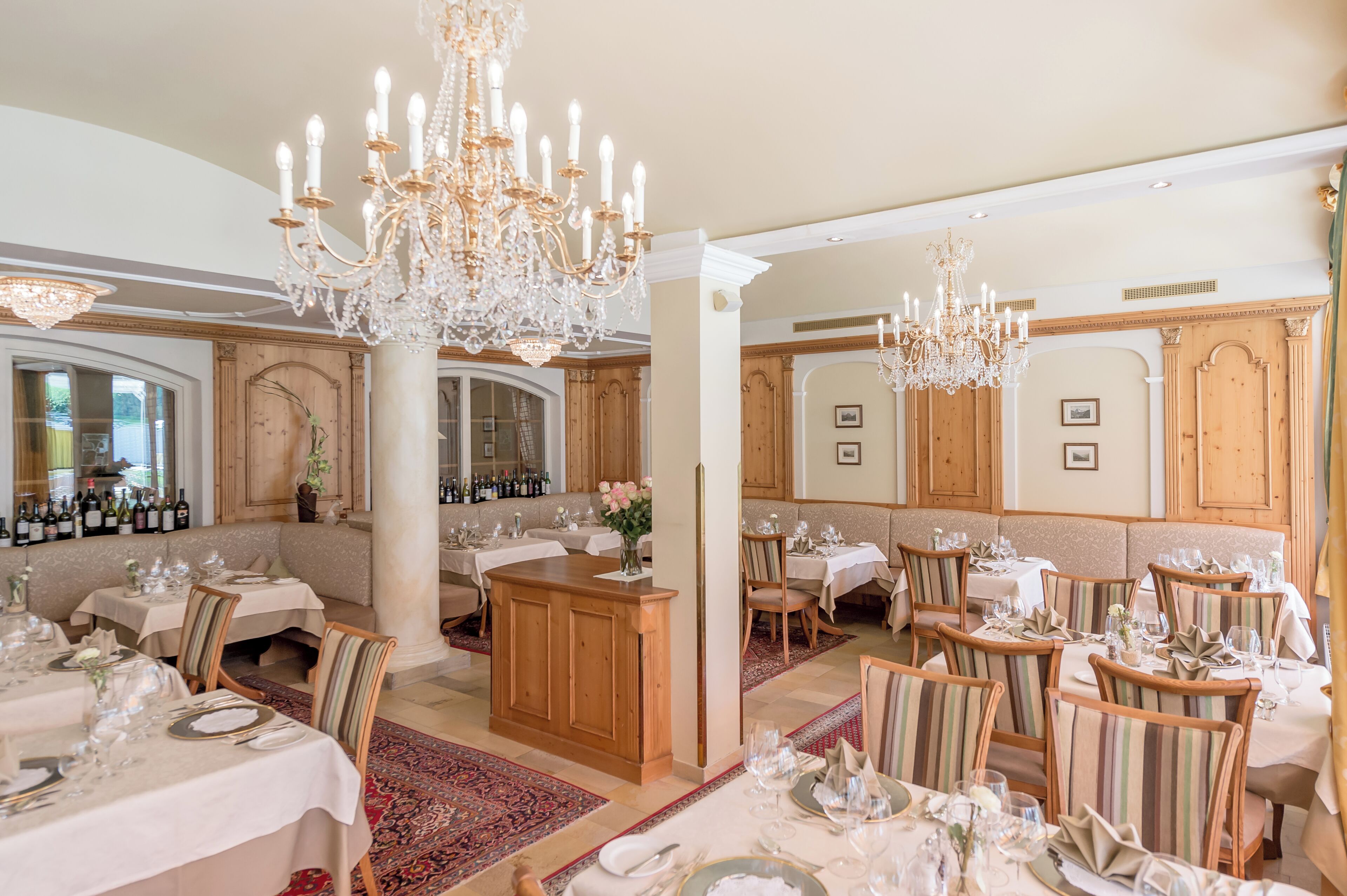 A formal dining room with chandeliers, wooden paneling, and neatly set tables.