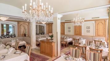 A formal dining room with chandeliers, wooden paneling, and neatly set tables.