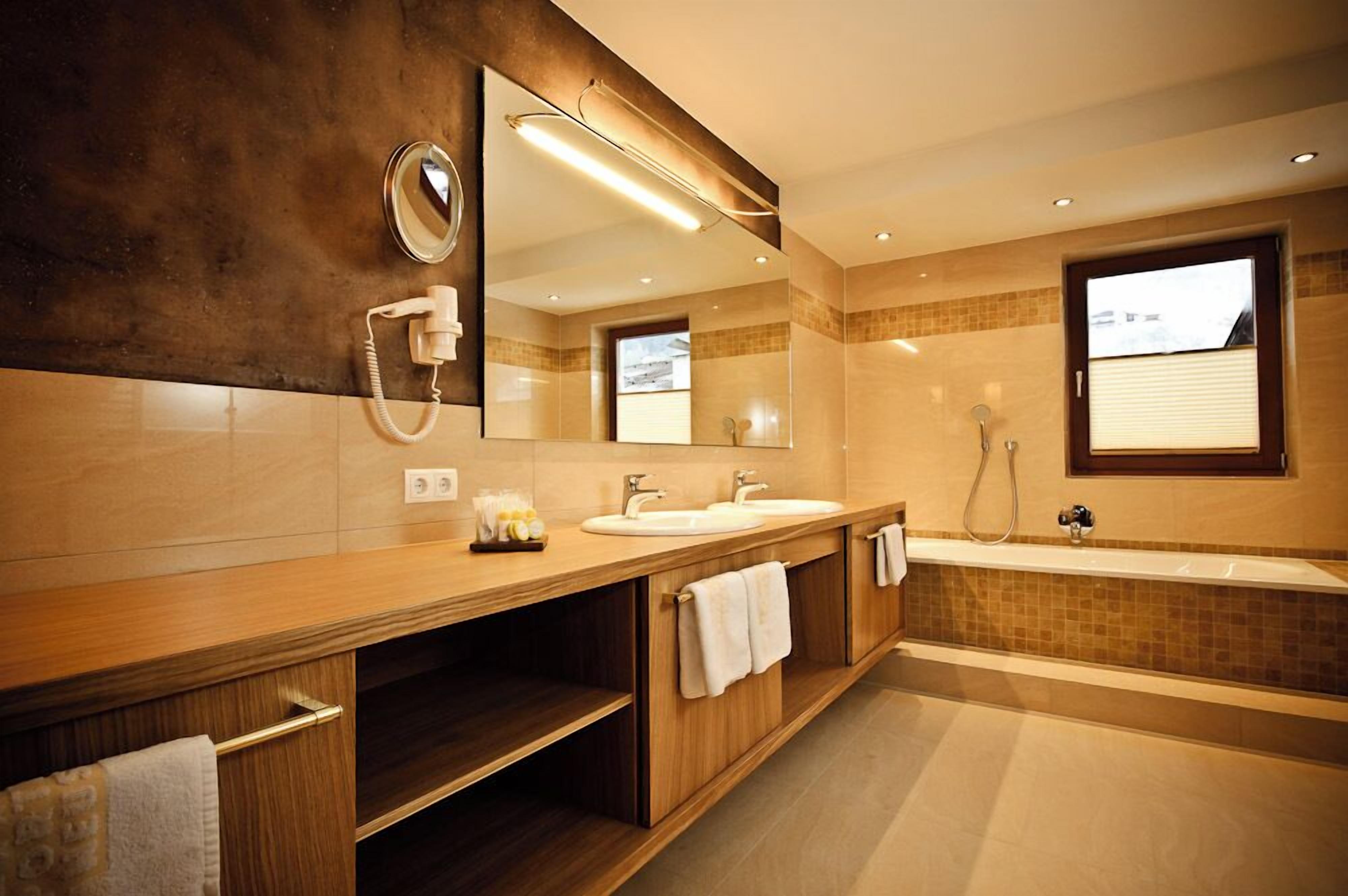 A modern bathroom with a large mirror, two sinks, a bathtub, and a shower.
