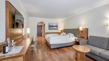 A hotel room with a bed, a sofa, a small table, a desk with a mirror, and a picture on the wall.
