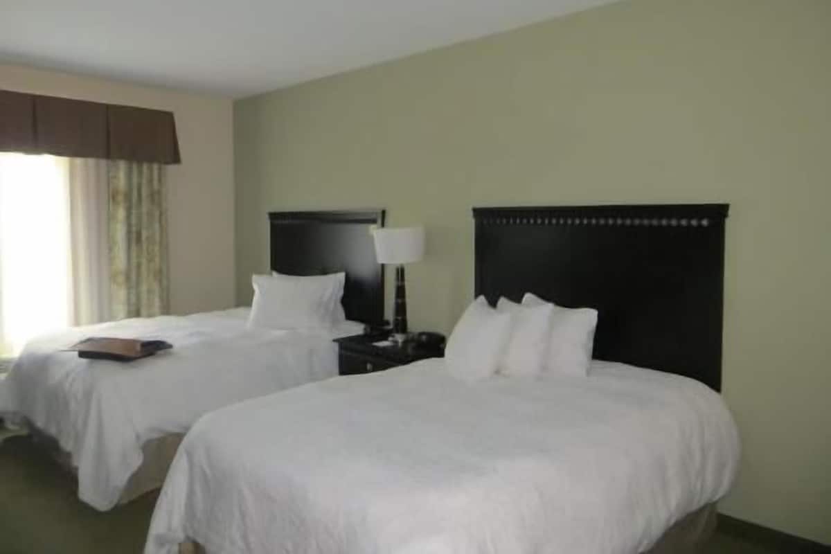 A hotel room with two beds, a nightstand with a lamp, and a window with curtains.