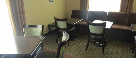 A hotel room with a dining area featuring a table and chairs, a sofa, and a carpeted floor.