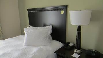 A neatly made bed with white linens, a black headboard, and a bedside table with a lamp, phone, and a small clock.