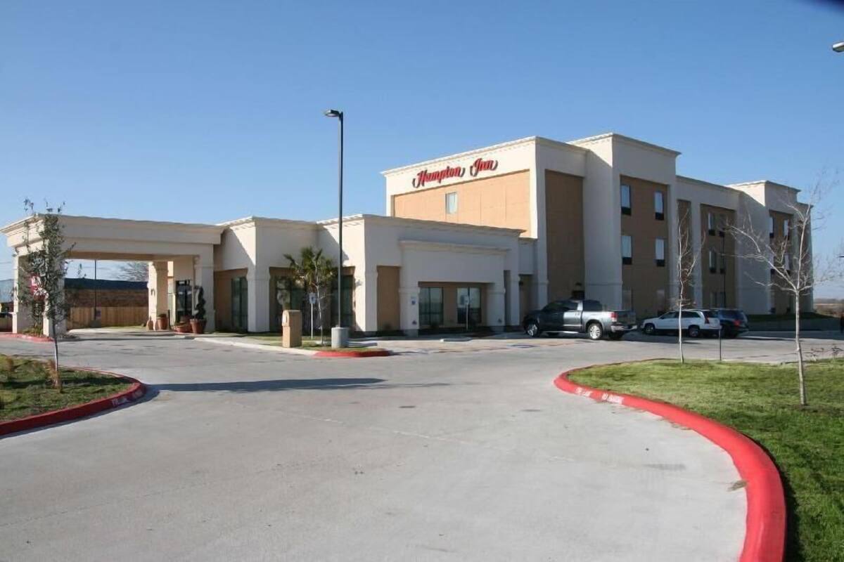A Hampton Inn hotel with a modern design, featuring a large parking lot and a clear sky.