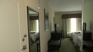 Habitación de hotel con cama, escritorio, silla, televisor y espejo.