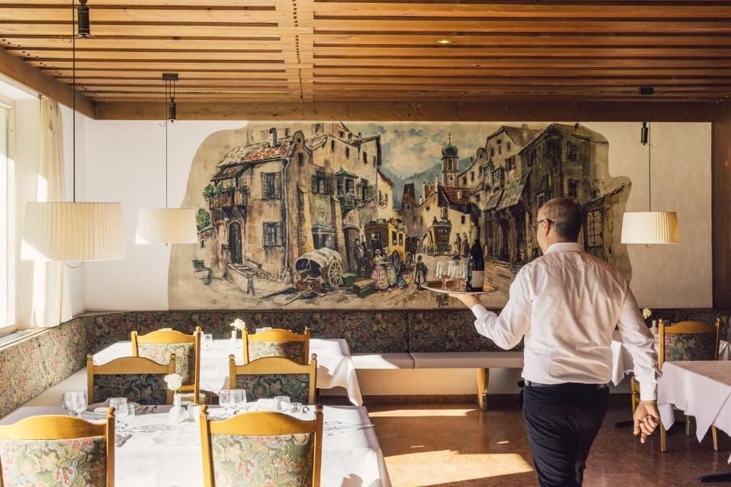 A restaurant with a mural of a street scene, wooden ceiling, and tables set for dining.