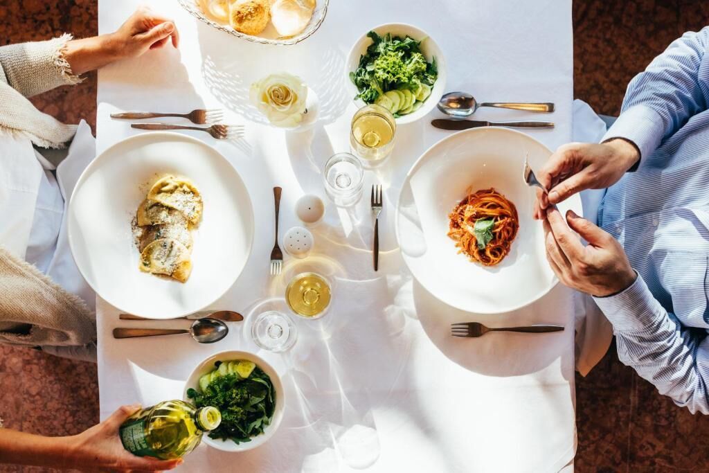 Una mesa de comedor con platos de comida, cubiertos y copas de vino.