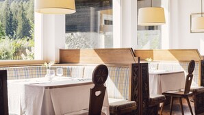 A dining area with a wooden bench, white tablecloths, and hanging lamps. - Posthotel (Valle Aurina)