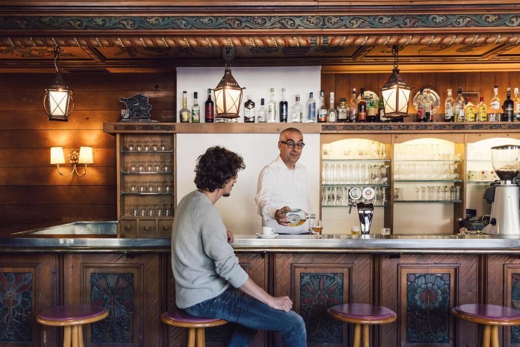 Angolo bar con rivestimenti in legno, sgabelli da bar e diverse bottiglie e bicchieri sugli scaffali.