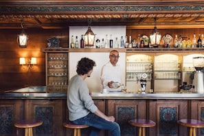 Zona de bar con paneles de madera, taburetes y una variedad de botellas y vasos en estantes.