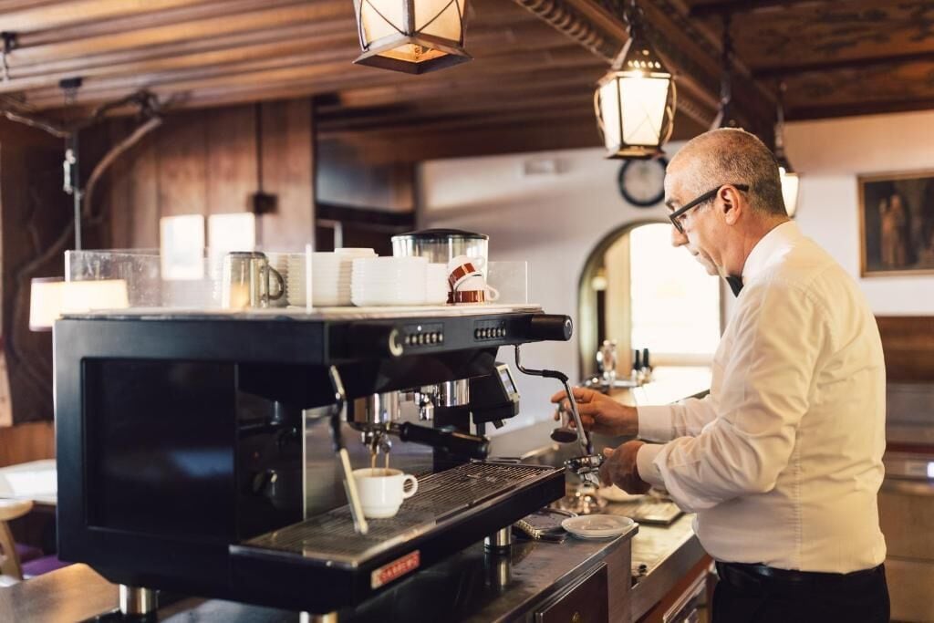 A barista at work in a cafe with a coffee machine, cups, and a counter.