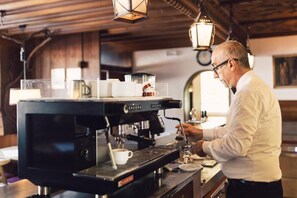 A barista at work in a cafe with a coffee machine, cups, and a counter. - Posthotel (Valle Aurina)