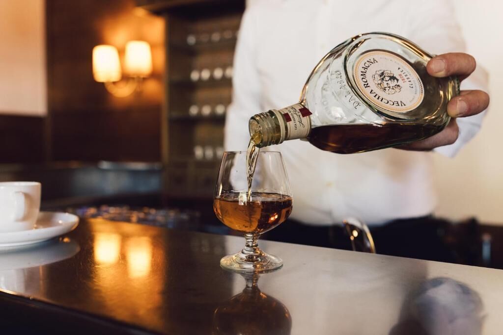 A person pouring a dark liquid from a bottle into a glass.