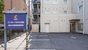 Comfort Hotel -kyltti, aidattu pysäköintialue ja rakennus, jossa on useita ikkunoita ja ulkoportaat.