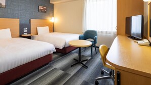 Hotellihuone, jossa on kaksi sänkyä, työpöytä, jossa on televisio, tuoli ja pieni pöytä.