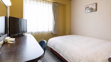 A hotel room with a bed, a desk with a television and phone, a chair, and a window with curtains.