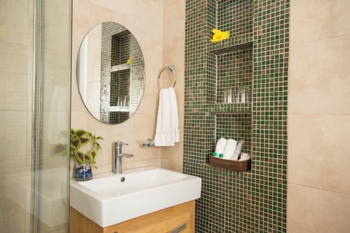 A bathroom with a sink, mirror, towel ring, and a shelf with toiletries.