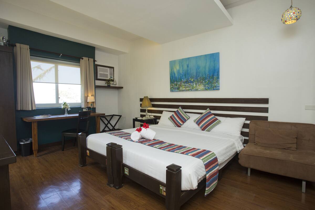 Habitación de hotel con una cama grande, un escritorio, una silla, un sofá y un cuadro en la pared.
