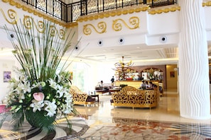 A lobby with a reception desk, seating areas, and decorative elements like a large floral arrangement.
