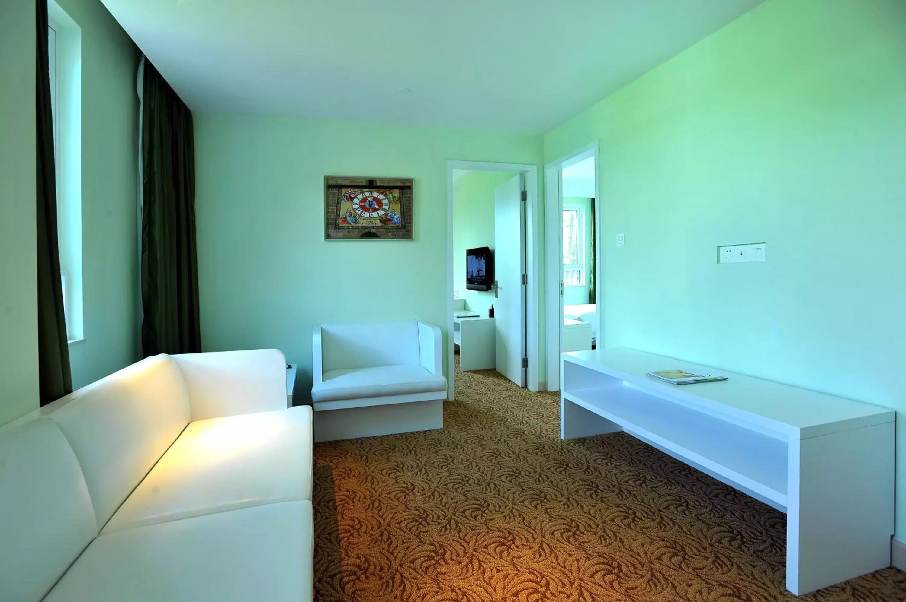 A hotel room with a white sofa, a white console table, a patterned carpet, a clock on the wall, and a television in the background.