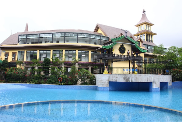 A hotel with a swimming pool, a large building with a curved roof, and a tower with a pointed roof.