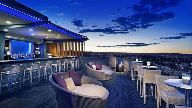 A rooftop bar with wicker furniture, a bar counter, and a city view. - Hilton Windhoek (Windhoek)
