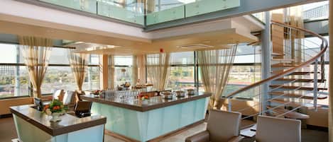 A spacious lobby with a central bar area, seating arrangements, and a prominent staircase.