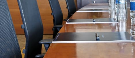 A conference room with a long table, black chairs, water bottles, and a projector screen.
