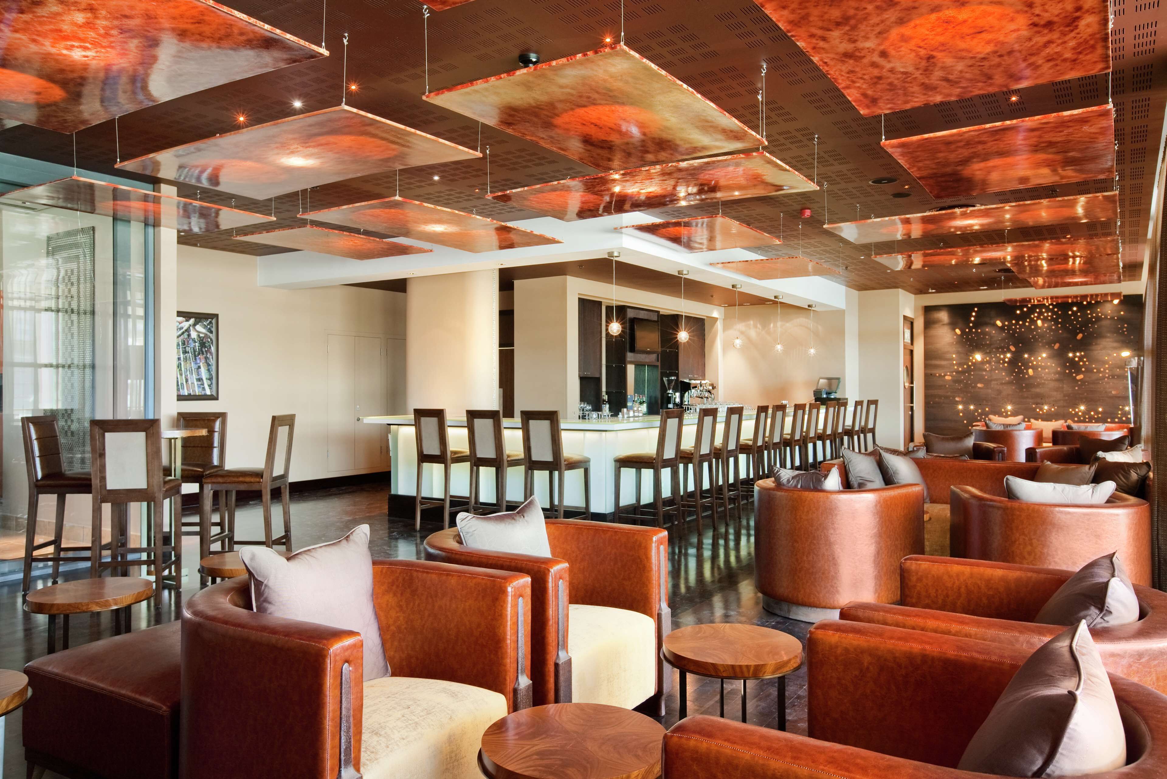A modern lounge area with leather sofas, wooden tables, and a bar in the background.