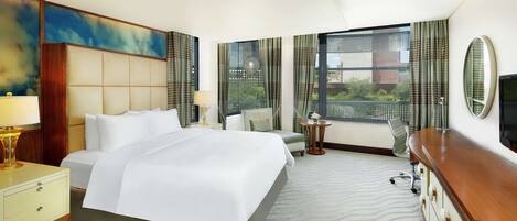 A hotel room with a large bed, a desk, a chair, a TV, and a window with curtains.