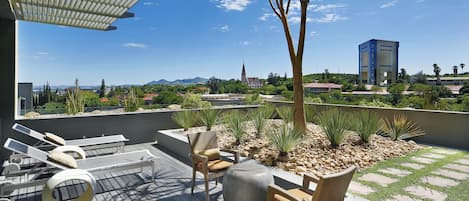 A rooftop terrace with outdoor furniture, a pergola, and a view of a church and mountains.