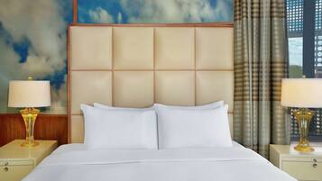 A hotel room with a large bed, two bedside tables with lamps, a headboard, and a window with curtains.