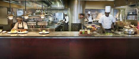 A professional kitchen with stainless steel appliances, a polished granite countertop, and chefs preparing food.