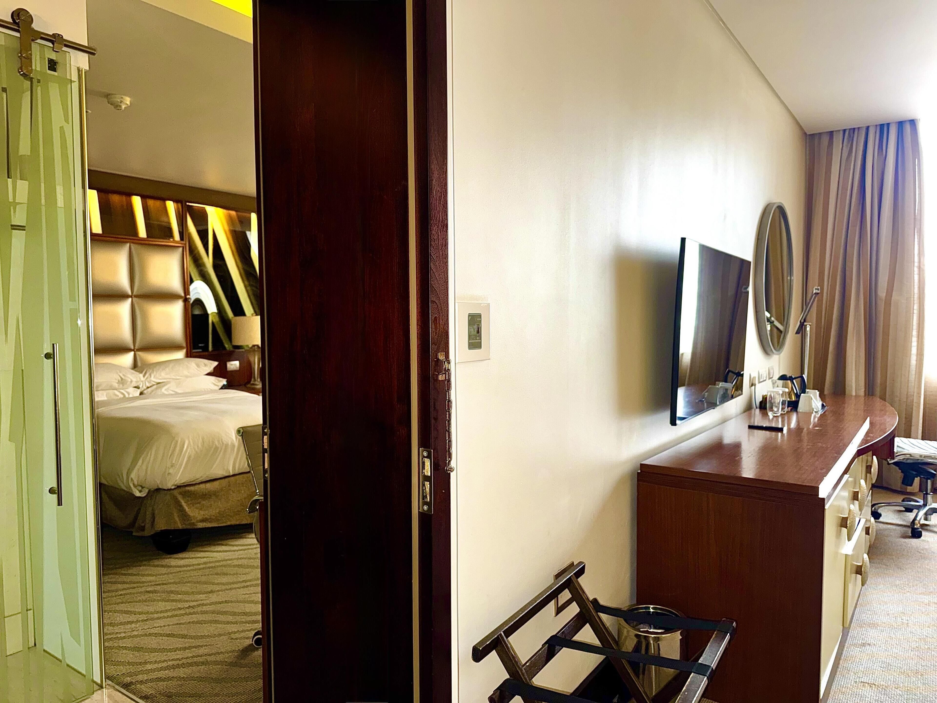 A hotel room with a bed, a desk, a mirror, and a window with curtains.