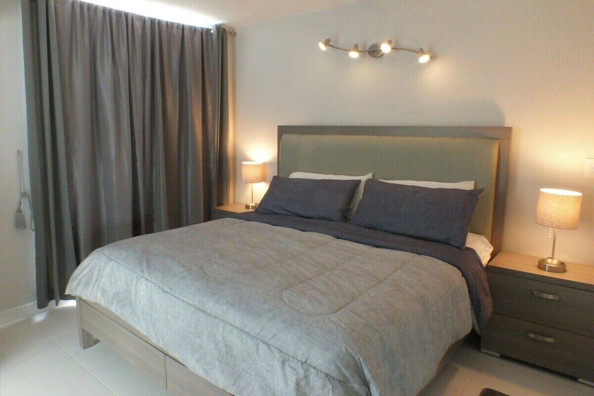 A modern bedroom with a large bed, two bedside tables, and a wall-mounted light fixture.