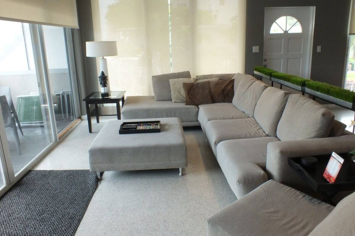 A modern living room with a grey sofa, a grey ottoman, and a small side table with a lamp.